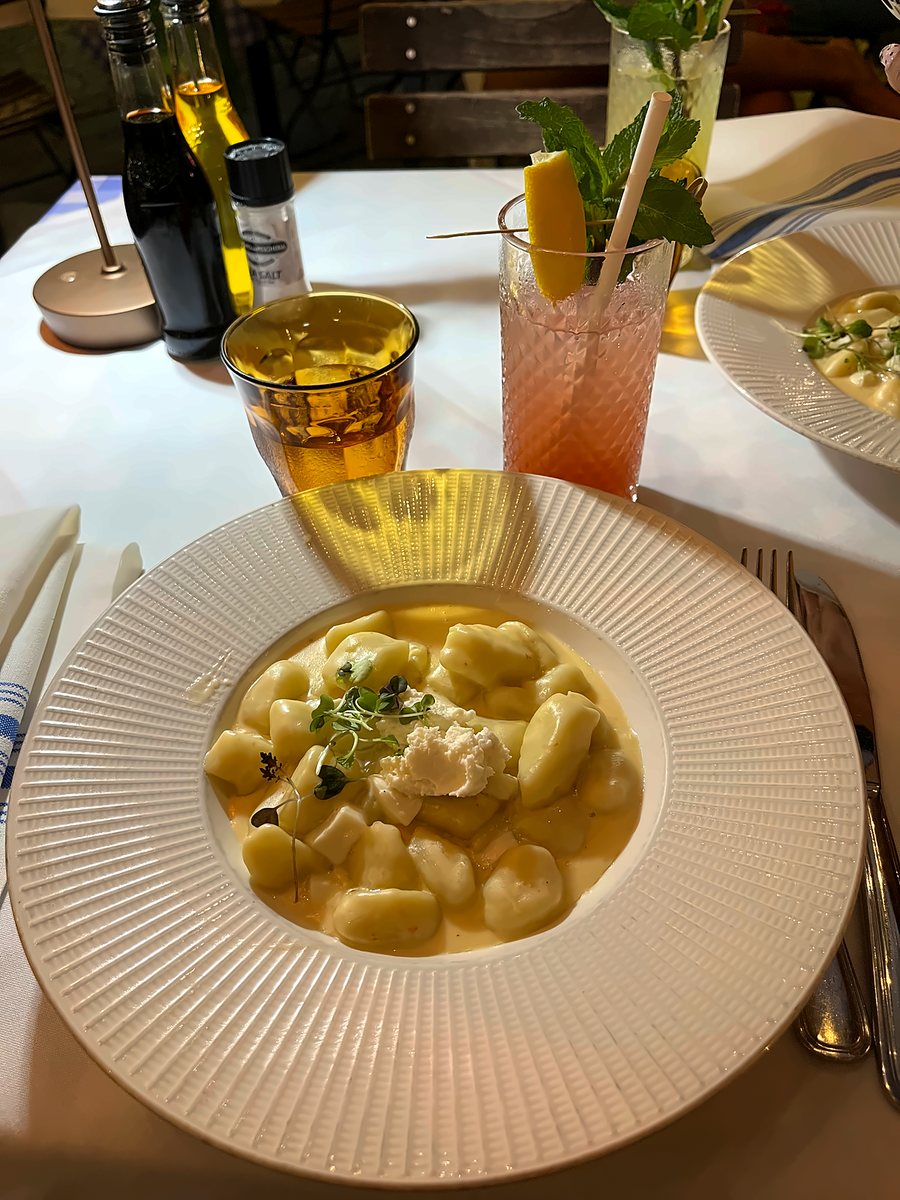 Plato de ñoquis en salsa blanca con tragos sobre una mesa